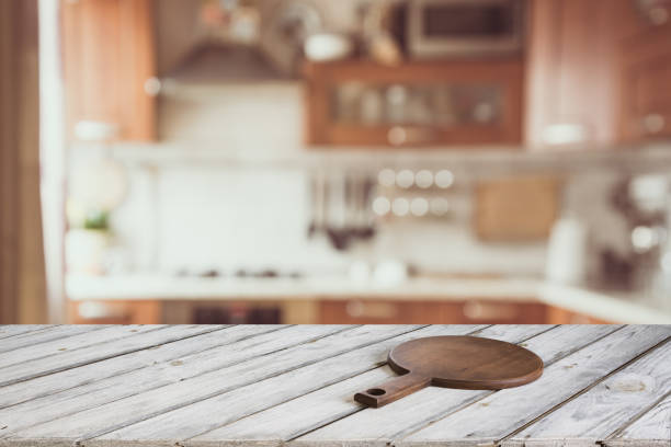 istock Blurred and abstract kitchen background. Empty wooden tabletop with cutting board  and defocused modern kitchen for display or montage your products. 807624590