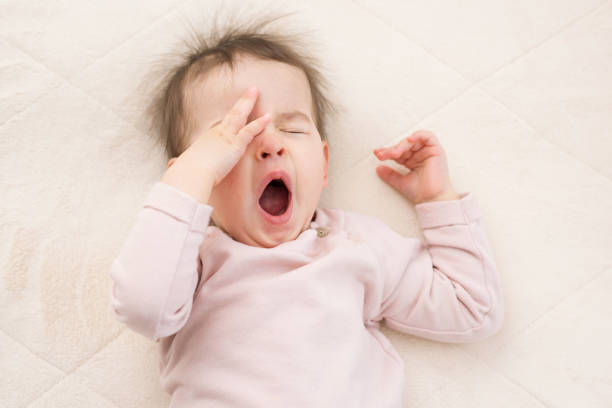 Portrait of sleeping beautiful and yawning baby toddler on the bed wearing pink pullover.  Bedtime. Nursery stock photo