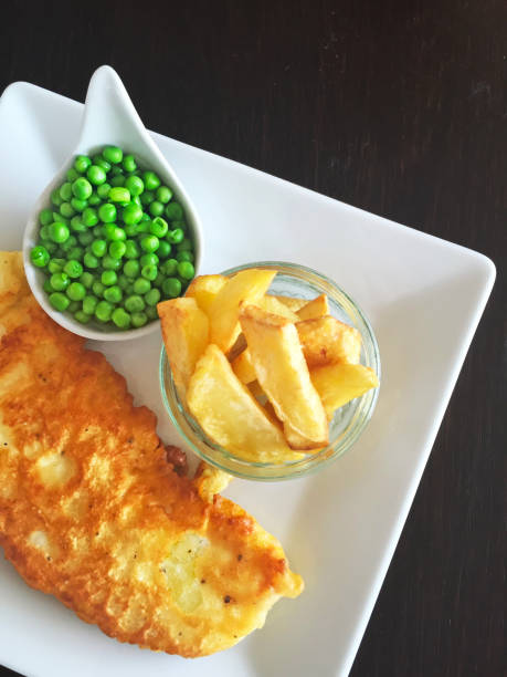 Fish and Chips with green peas on white plate.