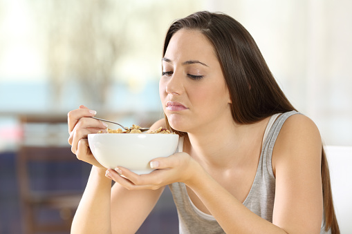 Disgusted woman eating cereals with bad taste at home