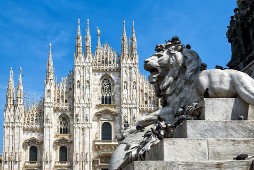 Sculpture of a lion as part of the monument to Victor Emanuel II in the Piazza del Duomo in Milan, Italy. The Milan Cathedral (Duomo di Milano) in the background.