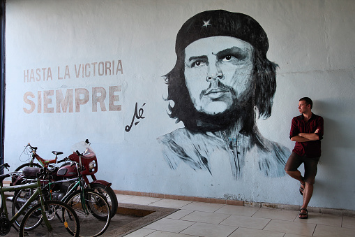 Tourist stands next to wall mural with revolution propaganda on February 22, 2011 in Sancti Spiritus, Cuba. Revolution propaganda is promoted by national government.