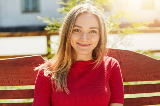 positiva guapa mujer con cabello rubio recta y pura piel mirando directamente a cámara sonriendo con hoyuelos en las mejillas admirando de tiempo soleado. concepto de la gente, estilo de vida, juventud y resto - dimple fotografías e imágenes de stock