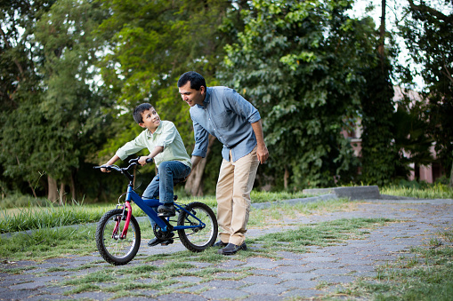 A mid adult latin father helping his son on his bicycle.