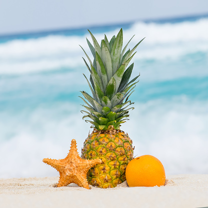 Pineapple, orange fruit and starfish on sand against turquoise caribbean sea water. Tropical summer vacation concept