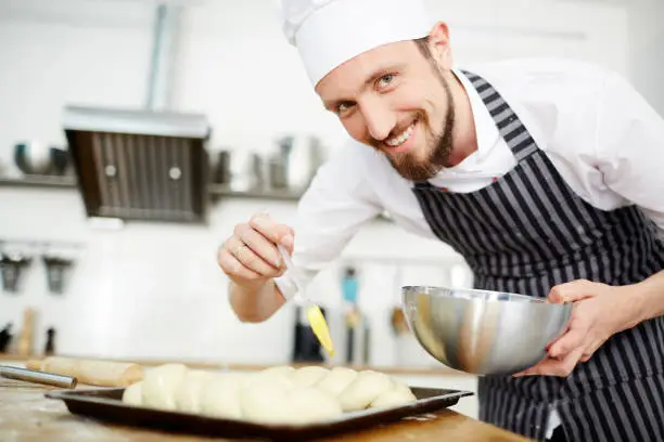 Happy man in chef uniform preparing loaves for baking