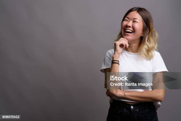 Studio Shot Of Young Asian Woman Wearing White Shirt Against Gray Background Stock Photo - Download Image Now