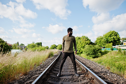 Cool black african american man in sunglasses walking and posing on railway in the countryside.