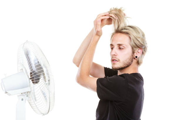 istock Young man fighting with wind from cooling fan 808117408