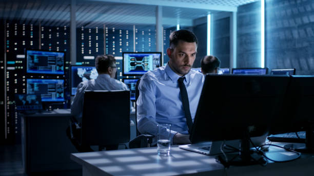 istock Close-up of Technical Engineer Working on His Computer With Multiple Displays in Monitoring Room. In the Background His Colleagues with Graphics and Various Data on Their Monitors. 808155054