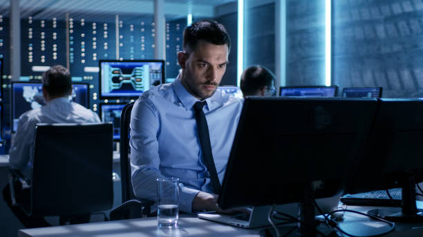 istock Close-up of Technical Engineer Working on His Computer With Multiple Displays in Monitoring Room. In the Background His Colleagues with Graphics and Various Data on Their Monitors. 808155066