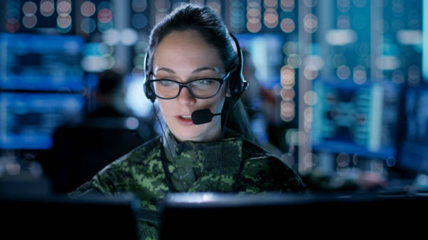 여성 it 엔지니어 정부 감시 기구에서 그녀의 데스크탑 컴퓨터에서 작동. 그들의 워크스테이션 그래픽을 보여주는 여러 스크린에 배경 사람들. - military technology 뉴스 사진 이미지