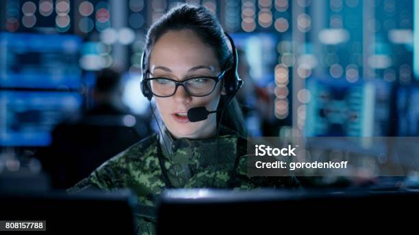 Female It Engineer Works On Her Desktop Computer In Government Surveillance Agency In The Background People At Their Workstations With Multiple Screens Showing Graphics Stock Photo - Download Image Now