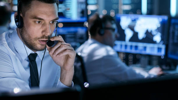 in monitoring room technical support specialist speaks into headset. his colleagues are working in the background. - administrator telephone office support imagens e fotografias de stock