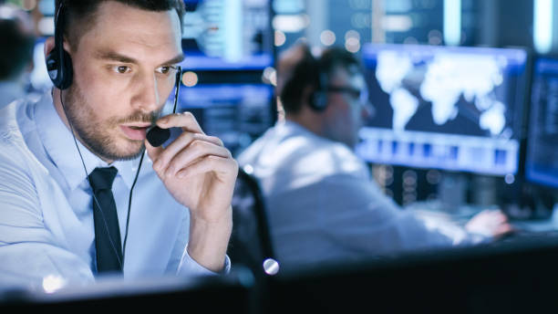 nella sala di monitoraggio lo specialista del supporto tecnico parla in cuffia. i suoi colleghi stanno lavorando sullo sfondo. - mittente foto e immagini stock