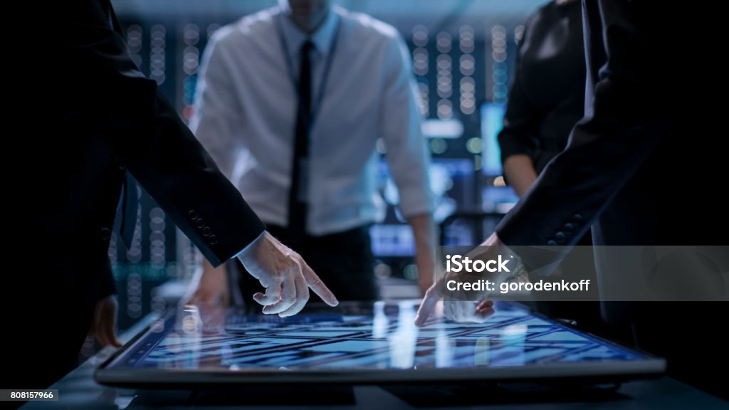 Gerentes corporativos trabalhando na mesa na sala de monitoramento. Quarto é cheio de tecnologia de ponta. Computadores com telas animadas. - Foto de stock de Decisão royalty-free