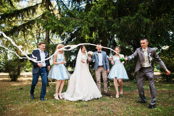 потрясающая свадебная пара с подружками невесты и женихами, пьющими шампанское в парке в идеальный солнечный день. - wedding reception wedding party bridesmaid стоковые фото и изображения
