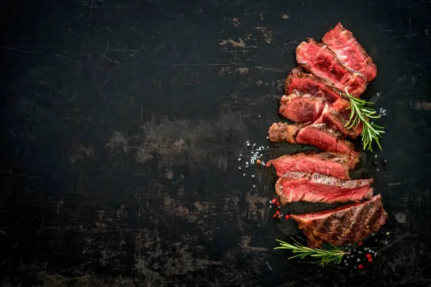 Sliced medium rare grilled beef ribeye steak on dark background