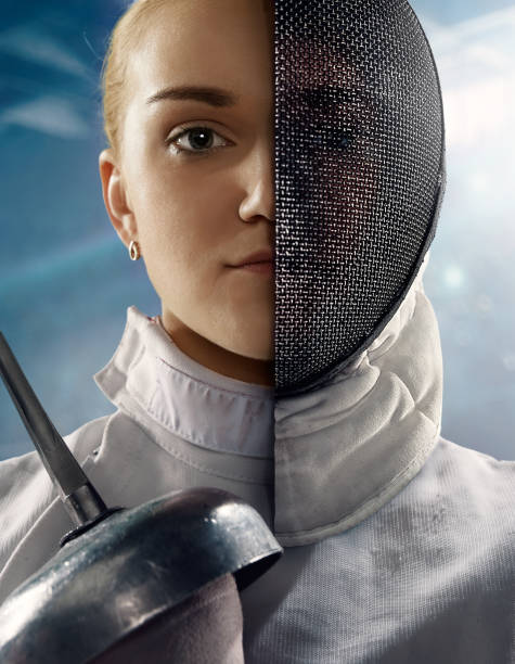 Fencer portrait with half face masked Fencer portrait with half face masked. The girl wears a white sports fencing suit, gloves, a protective helmet. She holds a sword in her hand. Half of the face is covered with a mask. face guard sport stock pictures, royalty-free photos & images