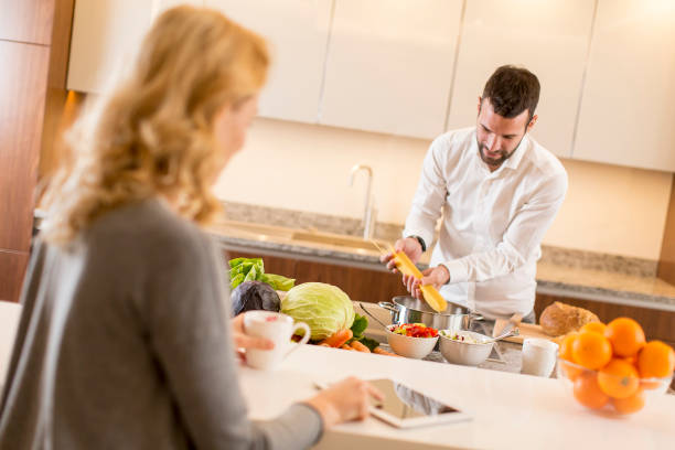 istock Man preparing a meal while a young woman sitting and use of tablets in a modern kitchen 808425682