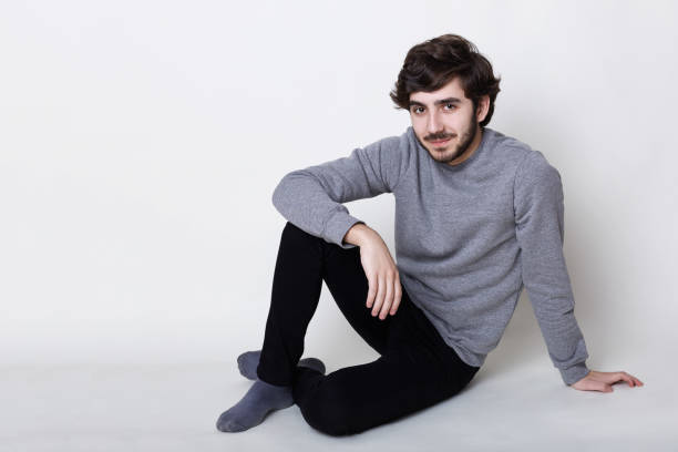 istock Good-looking pleased hazel-eyed boy with dark beard and moustache thick black eyebrows and stylish hairstyle wearing casual clothes sitting on the floor relaxing indoors having confident expression 808465632