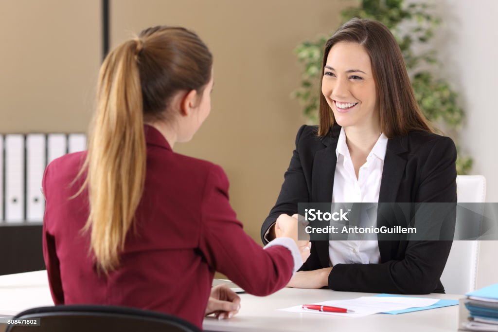 Two businesswomen handshaking at office Two businesswomen wearing suits handshaking after signing a contract of a good deal in an office interior Job Interview Stock Photo