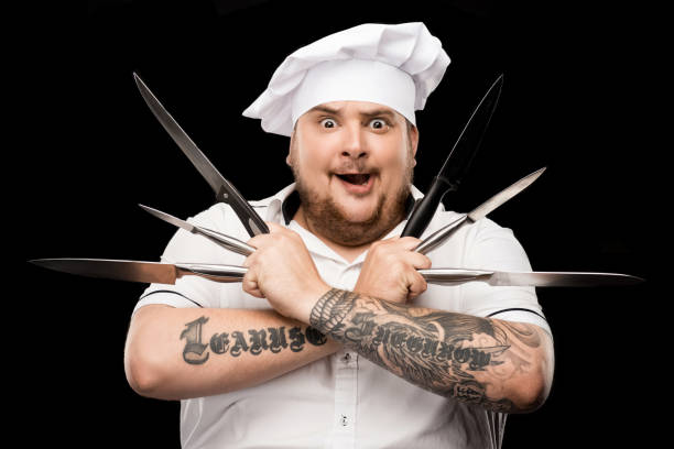 istock Excited young chef in hat and apron holding knives and looking at camera 808511352