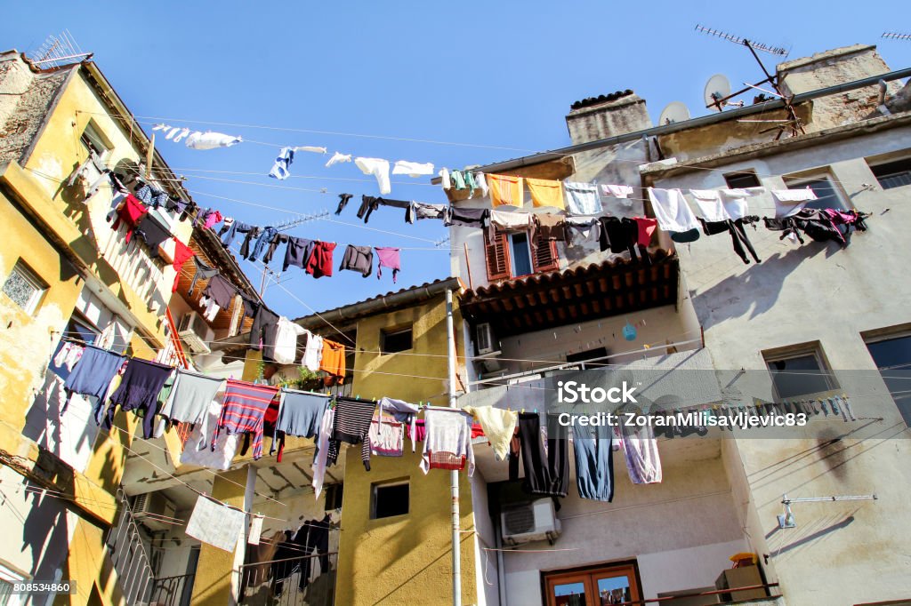 Laundry hanging on a clothes line on an old city building. Hanging Laundry and walls. Washing hanging on clothes lines between buildings. Drying clothes hanging outside the window of an old facade. Ancient Stock Photo