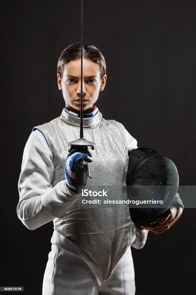Young woman fencer in white fencing costume Portrait of Young woman fencer wearing white fencing costume and holding sword and mask. Looking at camera. Black Background Fencing - Sport Stock Photo Young woman fencer in white fencing costume Portrait of Young woman fencer wearing white fencing costume and holding sword and mask. Looking at camera. Black Background Fencing - Sport Stock Photo