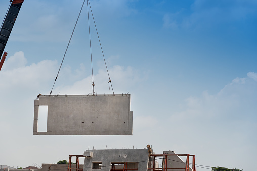 Construction site crane is lifting a precast concrete wall panel