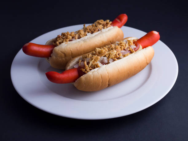 Two Danish hot dogs on white plate with black background