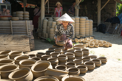 Hoi An ancient town, Quang Nam province, Vietnam - June 23, 2017 :  A woman working in pottery production base in Hoi An, Vietnam. She used clay to shape by hand out flower pots.