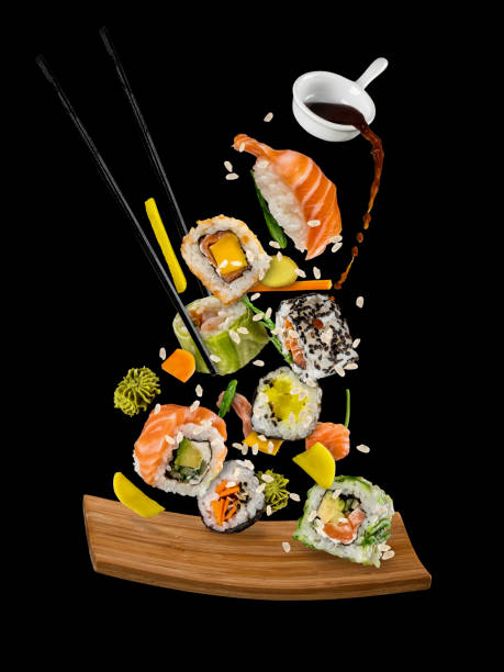 Sushi pieces placed between chopsticks on black background Sushi pieces placed between chopsticks, separated on black background. Popular sushi food. Very high resolution image maxi length stock pictures, royalty-free photos & images