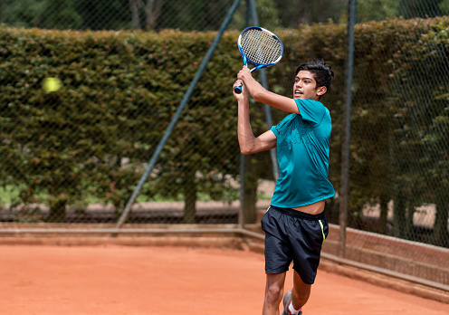 Young man playing tennis and hitting the ball with his racket â outdoors sports concepts
