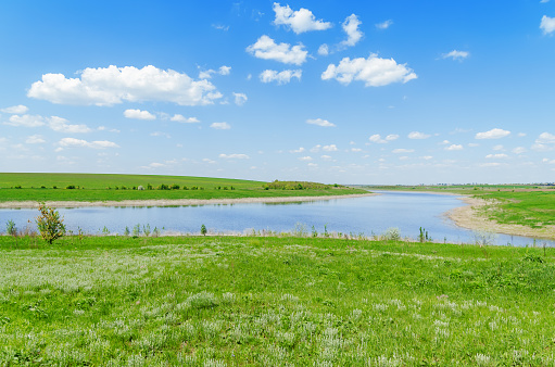 view of a river in green grass under a blue sky with clouds