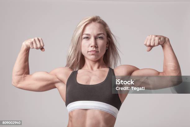 Athletic Young Blonde Woman Showing Bicep Muscles On The Soft Light Background Stock Photo - Download Image Now