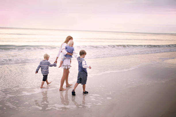 Mother and Children Walking Along Ocean Beach at Sunset A mother and her three young children, including a baby, are holding hands and walking along the ocean shore on a white sand beach in MarcoIsland, Florida at sunset. marco island stock pictures, royalty-free photos & images
