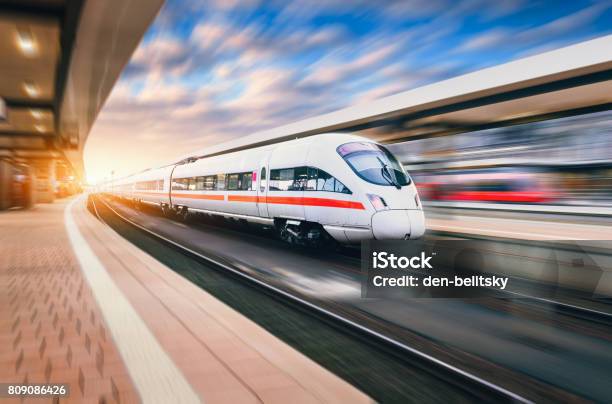 Witte Moderne Snelheid Trein In Beweging Op Treinstation Bij Zonsondergang Trein Op De Rails Van De Spoorweg Met Motion Blur Effect In Europa In De Avond Spoorlijn Platform Industriële Landschap Spoorlijn Toerisme Stockfoto en meer beelden van Trein