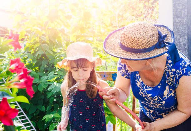 Mother and her little sun watering plants in garden in summer