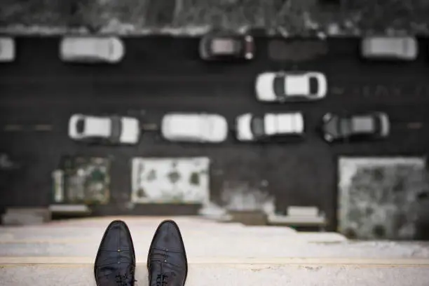 Photo of Close-up of man's feet standing on the edge of the roof. Top view on man's boots on the balcony of high building. Depression and instability concept. Crisis.