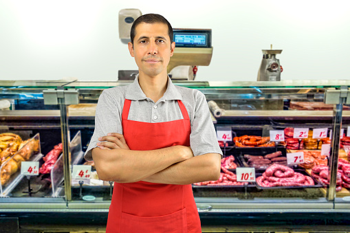 portrait of handsomemale butcher with arms crossed and smiling at the butchery