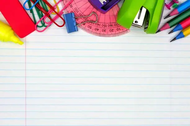 Photo of School supplies top border on lined paper background