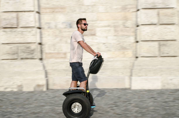 Panning on a man on segway with huge tire on sidewalk during summer day