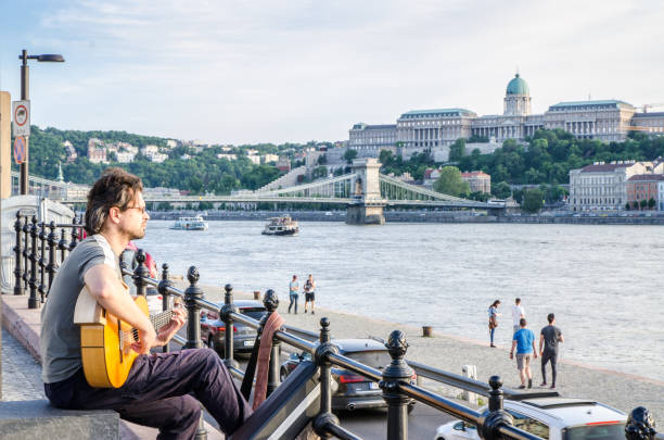 Man playing guitar while looking at the Budapest Danube river during summer day