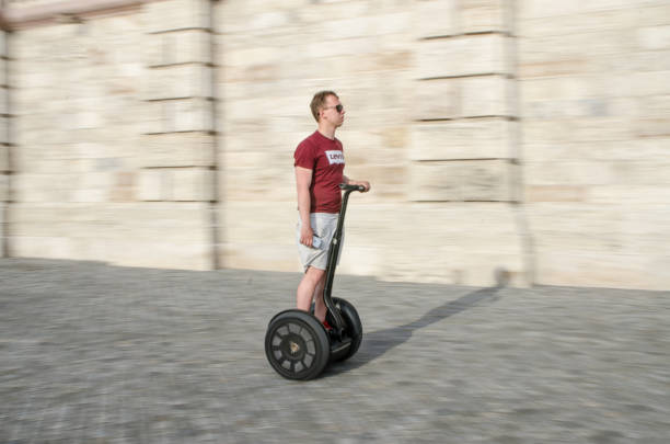 Panning on a man on segway with huge tire on sidewalk during summer day