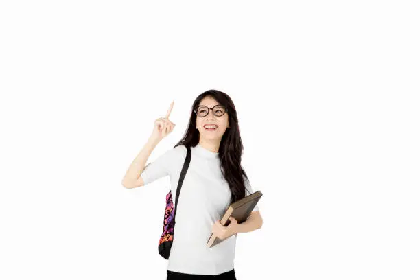 Portrait of Asian female college student smiling happy while pointing upward, looks gets an idea