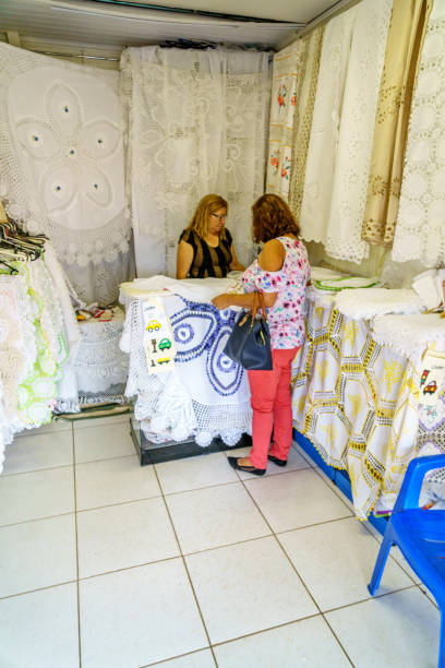 A market stall displaying a variety of traditional embroidered textiles, including tablecloths, napkins, and decorative fabrics. The intricate floral patterns and lace details showcase artisanal craftsmanship and cultural heritage. The vibrant colors and delicate embroidery create a visually rich and authentic scene.