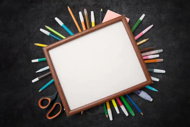 Top view of school supplies under a blank frame on the blackboard