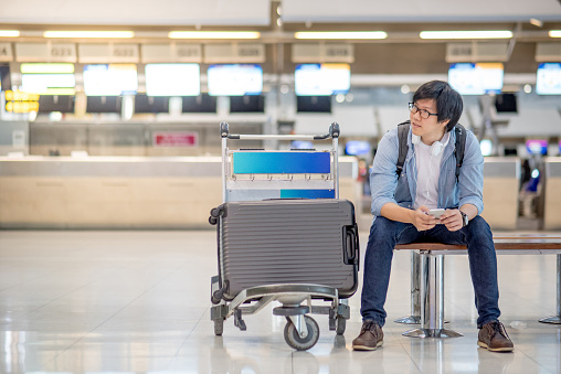 young asian guy waiting for check in and drop his luggage at airline check-in counter of international airport terminal