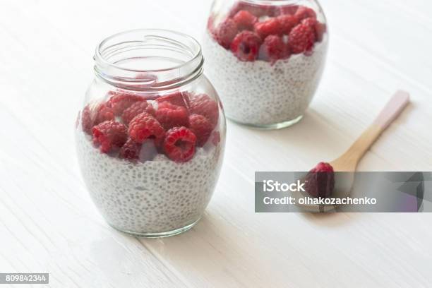 Chia Seeds Pudding With Coconut Milk And Raspberry In Glass Jars Wooden Spoon With Berry In White Wooden Table Concept Of A Healthy Diet Simlpe Breakfast Stock Photo - Download Image Now